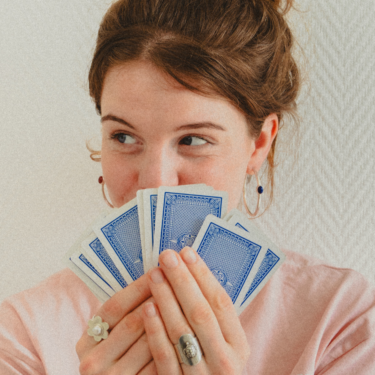 Woman holding playing cards in front of her face against a light background